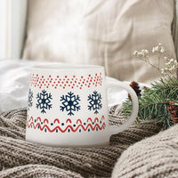 Decorative mug with snowflake pattern on a cozy blanket with greenery