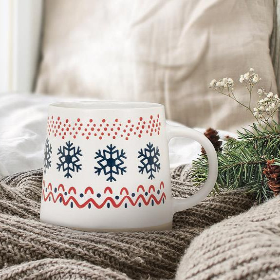 Decorative mug with snowflake pattern on a cozy blanket with greenery