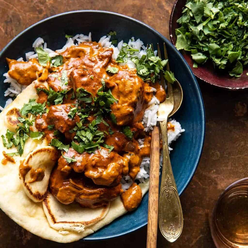 Bowl of curry with naan bread and a side of greens on a wooden table.