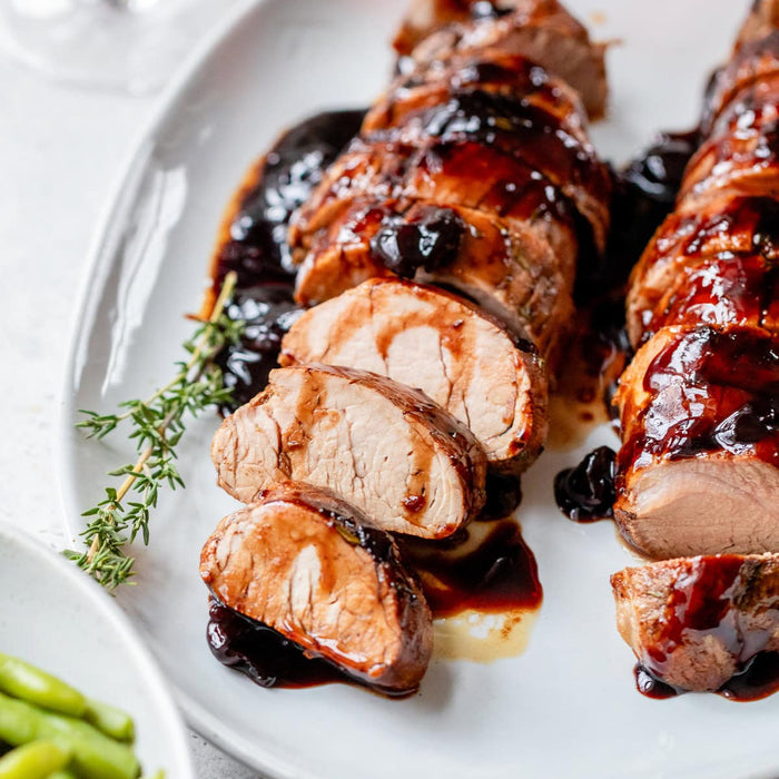 Sliced roasted pork tenderloin with a glaze on a white plate, accompanied by green beans.