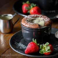 Chocolate souffle in a black ramekin with strawberries on a wooden table
