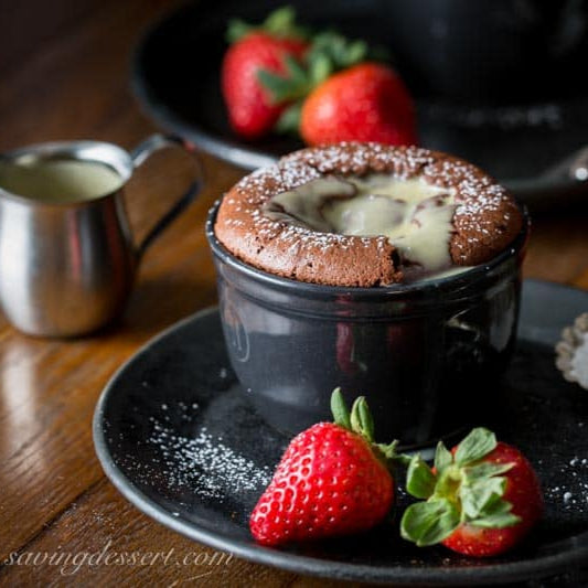 Chocolate souffle in a black ramekin with strawberries on a wooden table