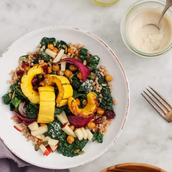 Two bowls of salad with squash, kale, and chickpeas on a marble surface.