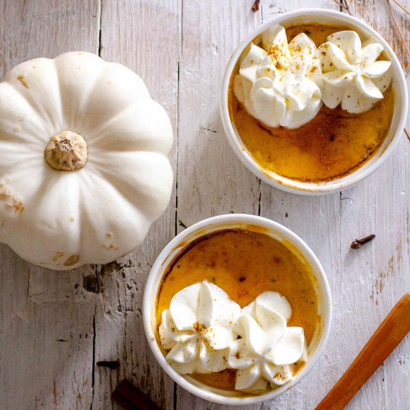 Pumpkin custard dessert with whipped cream in white bowls on a wooden surface.