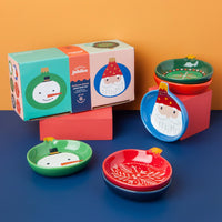 Set of Christmas-themed ceramic dishes with decorative designs on a blue surface against an orange background.