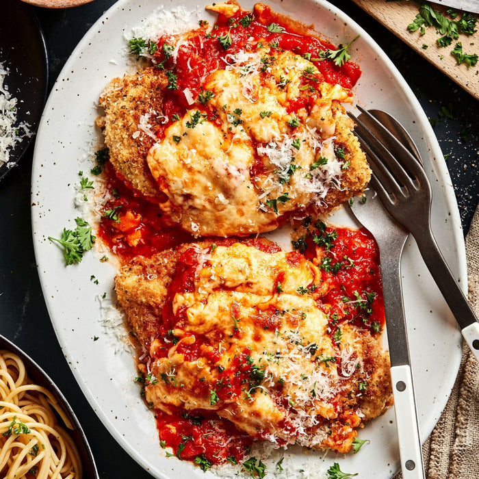 Plated dish of chicken parmesan with tomato sauce and cheese, served with a side of pasta.