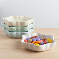 Set of ceramic bowls in pastel colors on a wooden surface with colorful candies.