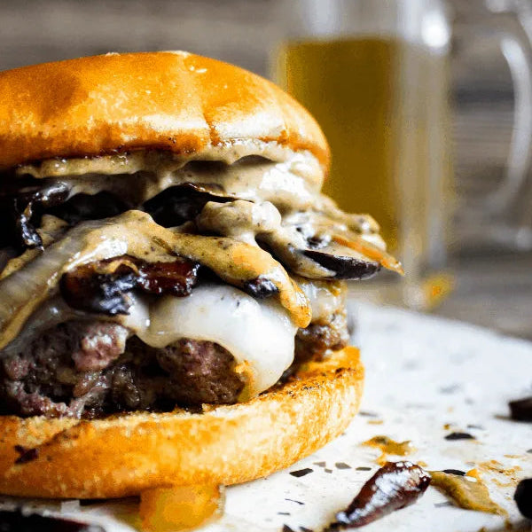 Hamburger with various toppings on a bun, served with a side of fries and a glass of beer in the background.
