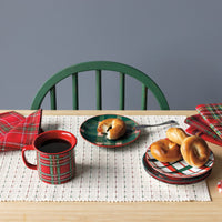 Dining table set with plaid tableware, plates, and a green chair against a gray wall.