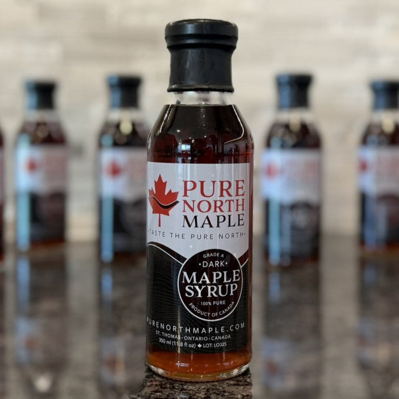 Bottle of Pure North Maple syrup on a reflective surface with smaller bottles in the background.