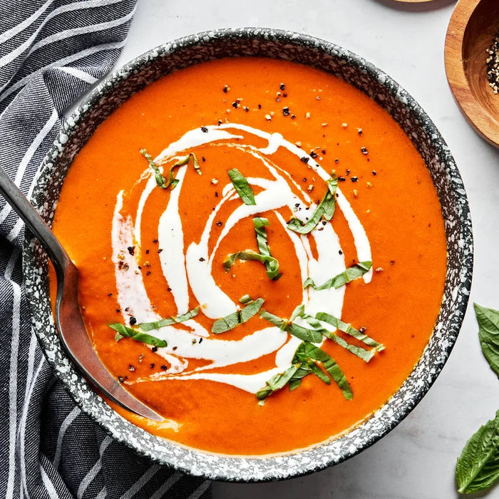 Bowl of tomato soup with cream and basil on a marble surface