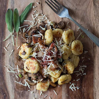 Wooden cutting board with a pasta dish topped with mushrooms and cheese, accompanied by a fork.