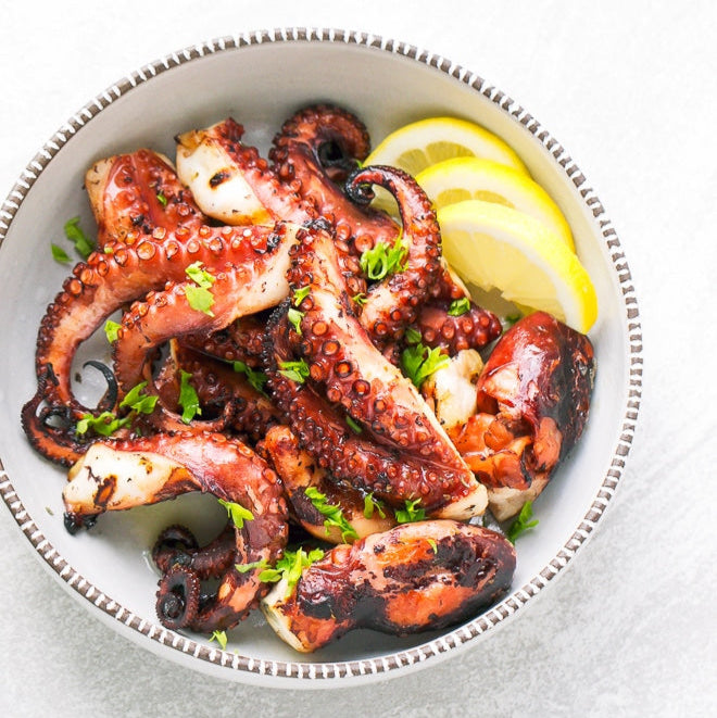 Grilled octopus with lemon wedges on a white plate
