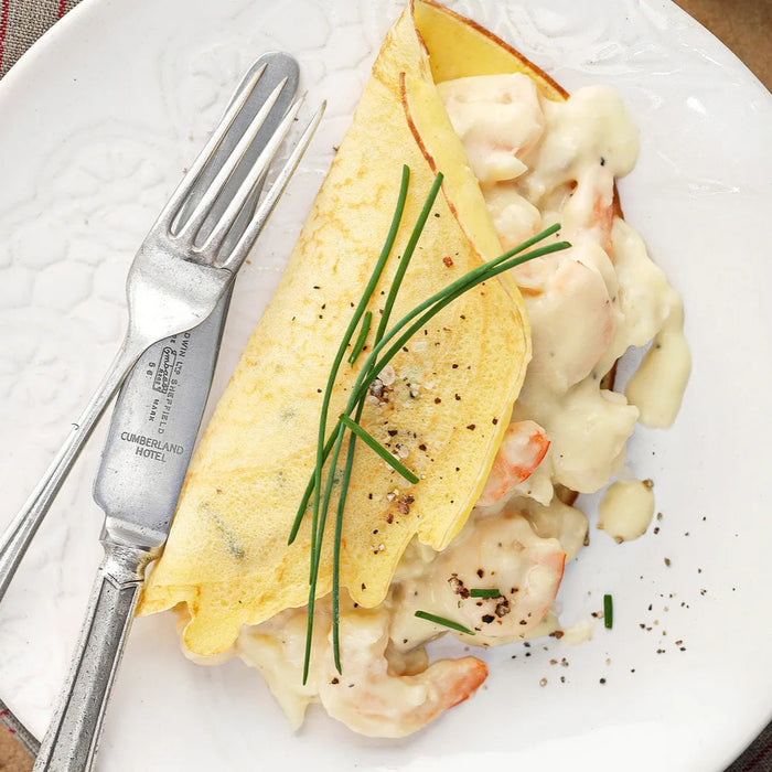 Seafood omelette on a white plate with a fork and knife, placed on a wooden table.