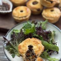 Small pie on a plate with salad, with more pies in the background