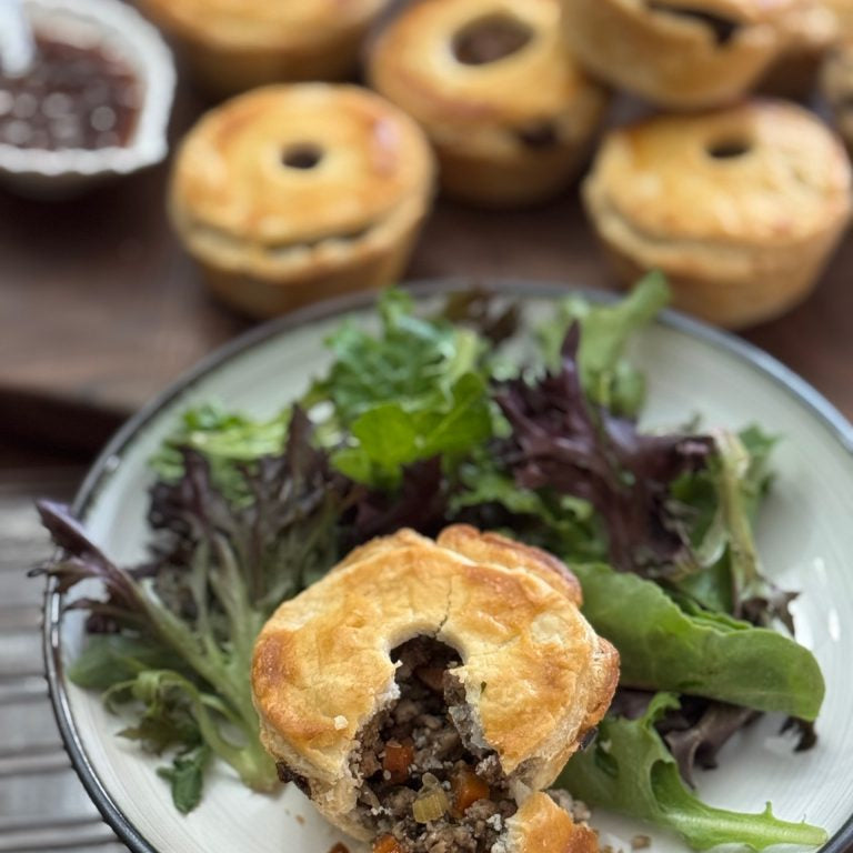 Small pie on a plate with salad, with more pies in the background